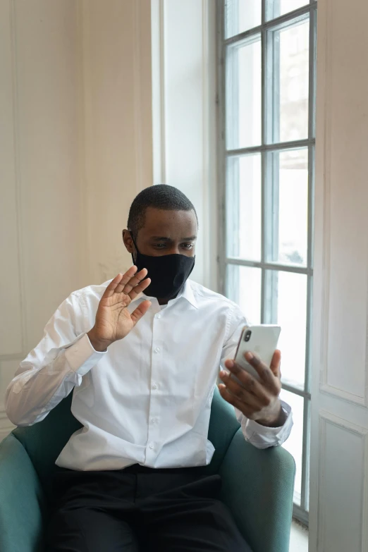 a man sitting in a chair using a cell phone, white man with black fabric mask, greeting hand on head, mkbhd, human staring blankly ahead