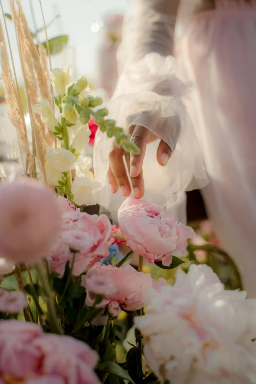 a close up of a person putting flowers in a vase, inspired by Oleg Oprisco, unsplash, bride, white and pink cloth, waving, display”