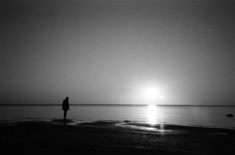 a person standing on top of a beach next to the ocean, a black and white photo, sun at dawn, taras susak, red sea, during the night