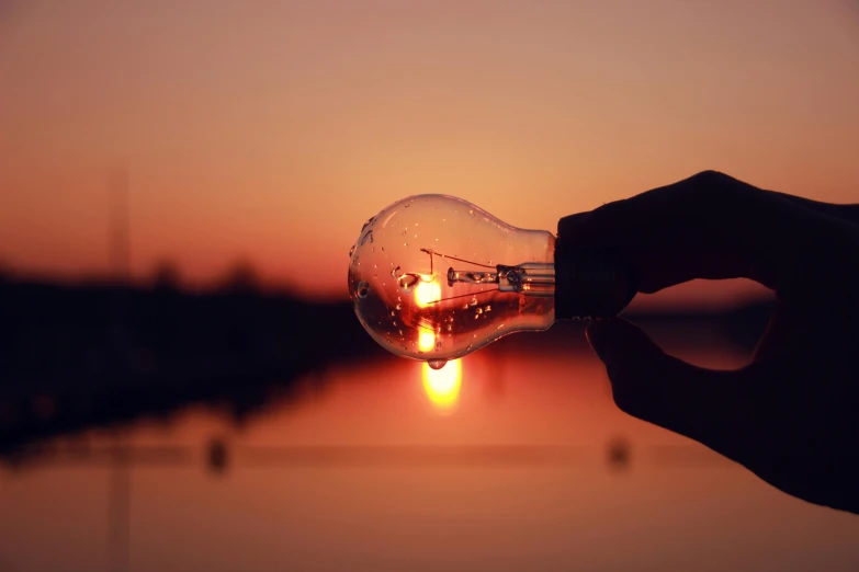 a person holding a light bulb with the sun setting in the background, by Jesper Knudsen, pexels contest winner, realism, street lights water refraction, instagram post, broken lights, screensaver