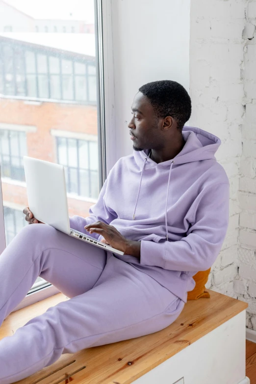 a man sitting on a window sill using a laptop, trending on pexels, renaissance, wearing a purple sweatsuit, pastel clothing, mkbhd, wearing pajamas