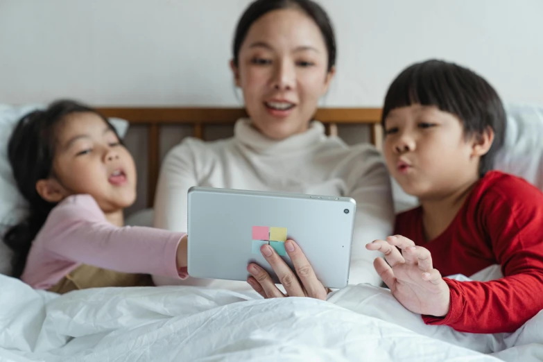 a woman sitting on top of a bed next to two children, a cartoon, pexels contest winner, using a magical tablet, asian descent, square, netflix