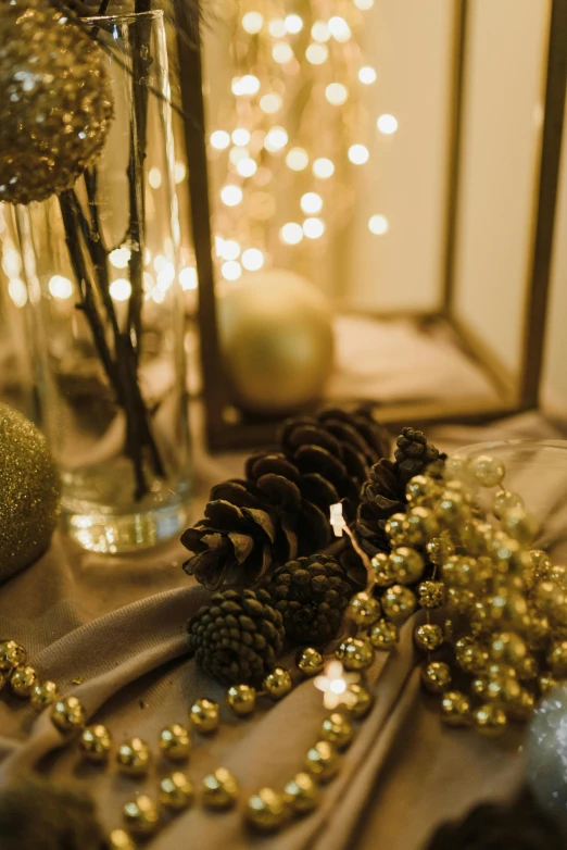 a table topped with a vase filled with pine cones, string lights, gold and luxury materials, medium close up