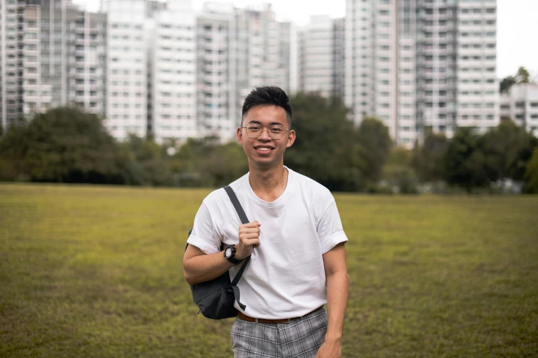 a man standing in a field with buildings in the background, a portrait, inspired by Reuben Tam, pexels contest winner, while smiling for a photograph, teacher, singapore, slightly pixelated