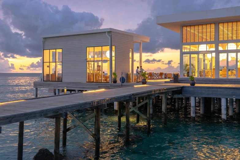 a couple of houses sitting on top of a pier, during a sunset, sol retreat, with glowing windows, eight eight eight