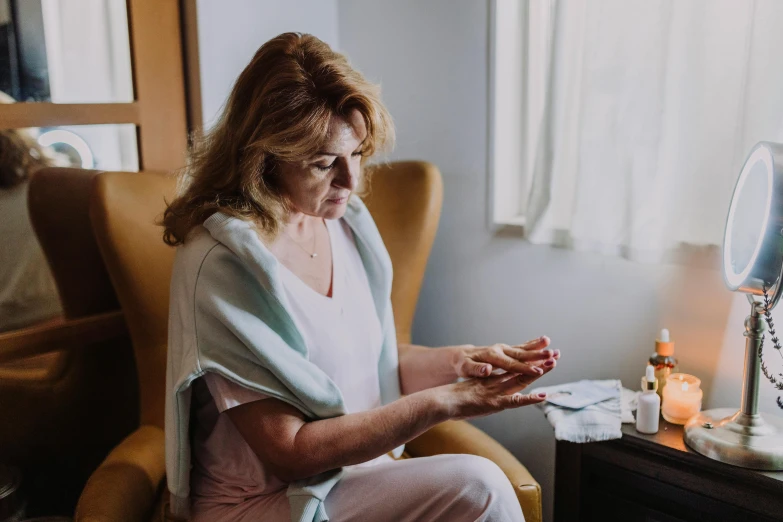 a woman sitting in a chair looking at her cell phone, by Julian Allen, pexels contest winner, wearing a hospital gown, holding a crystal ball, hands on counter, comforting