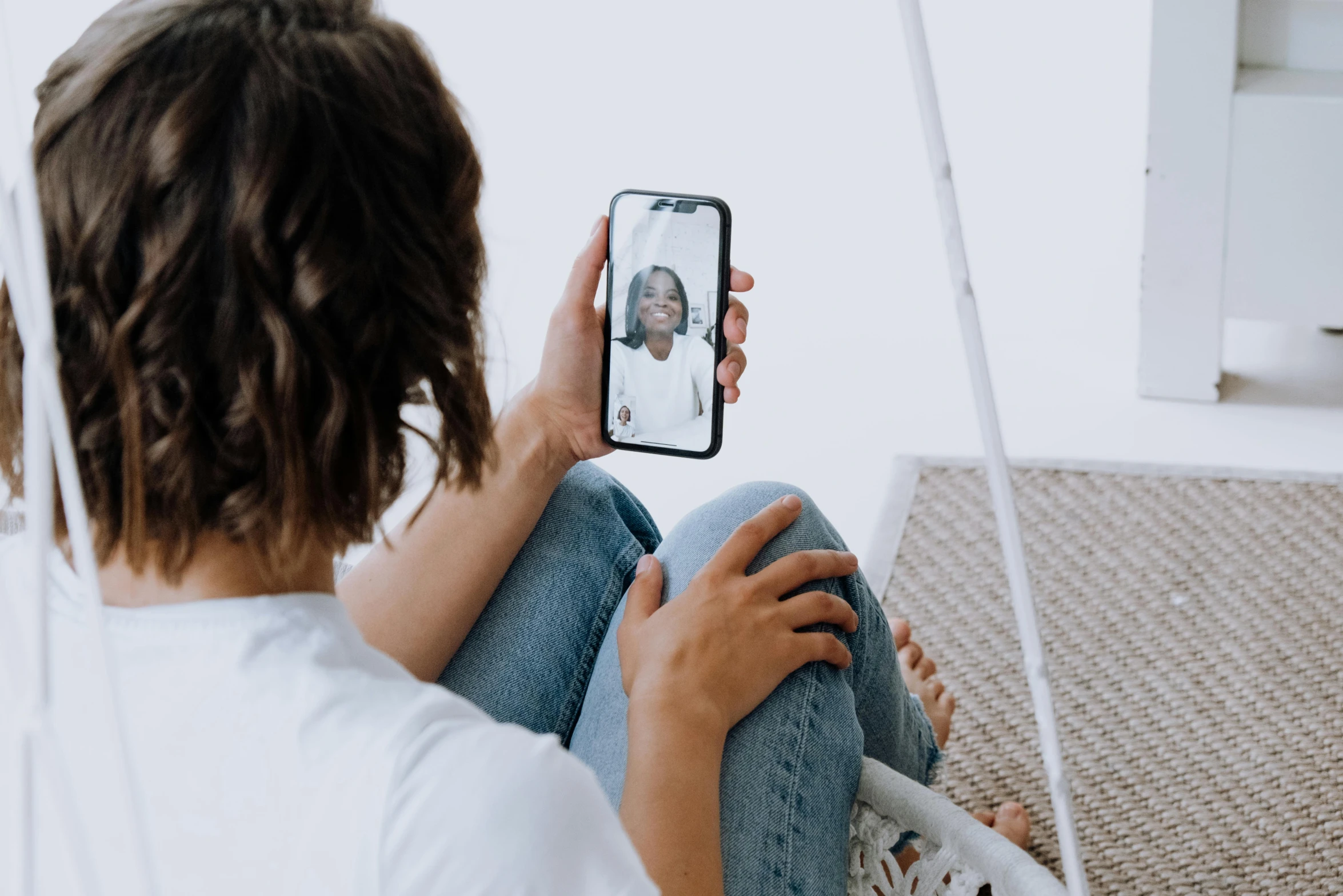 a woman taking a picture of herself on her phone, trending on pexels, with brown skin, dressed in a white t shirt, sitting in chair, long distance photo