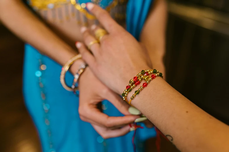 a woman putting a ring on another woman's finger, an album cover, pexels, hurufiyya, wearing a dress made of beads, red blue and gold color scheme, bracelets, thumbnail