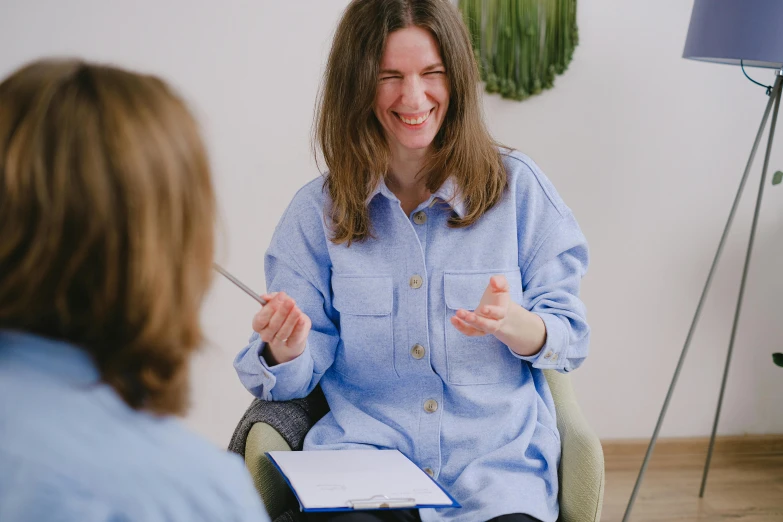 a woman sitting in a chair talking to another woman, earing a shirt laughing, colour corrected, thumbnail, neuroscience