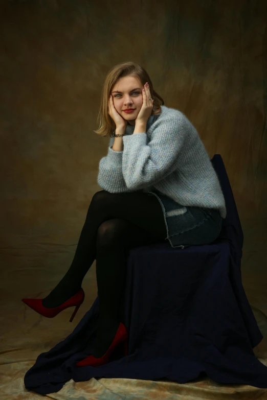 a woman sitting on top of a blue blanket, samara weaving, red sweater and gray pants, dark grey backdrop studio, on her throne