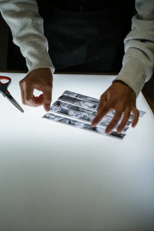 a person cutting a piece of paper with a pair of scissors, a silk screen, video art, cinematic counter light, digital image, analog photograph, educational