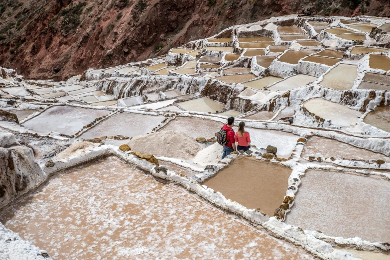 a woman sitting on the edge of a salt pan, process art, quechua, avatar image, tiny people walking below, terraces