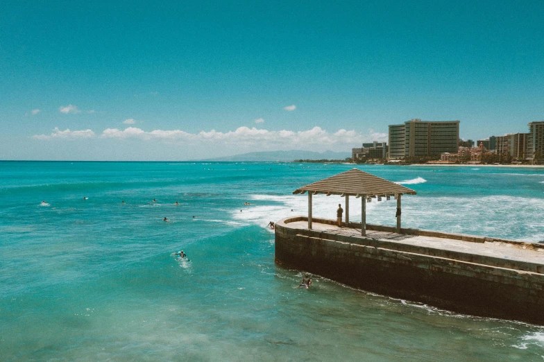 a gazebo sitting on top of a pier next to the ocean, pexels contest winner, waikiki beach skyline, people swimming, shades of blue, surfing