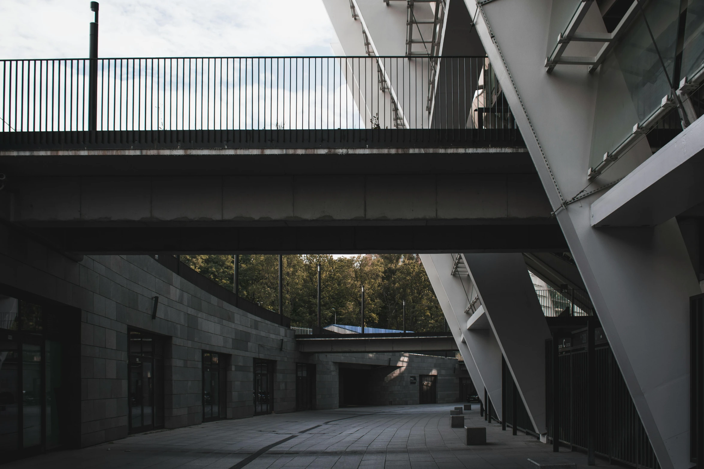 a black and white photo of a walkway between two buildings, inspired by Tadao Ando, pexels contest winner, stadium, white wall complex, metallic bridge, post - soviet courtyard