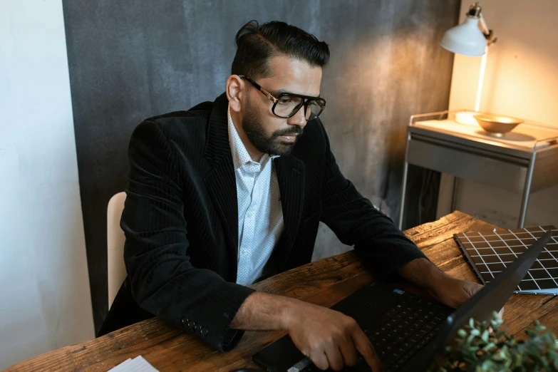 a man sitting at a desk using a laptop computer, a screenshot, pexels contest winner, hurufiyya, wearing a suit and glasses, concentration, thumbnail, lachlan bailey