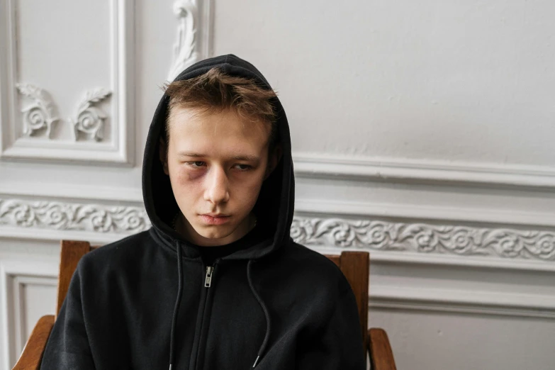 a young man in a black hoodie sitting in a chair, trending on pexels, hyperrealism, black eyed kids, bruised face, ilya golitsyn, seated in court