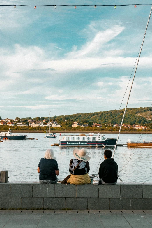 a group of people sitting next to a body of water, harbour, afternoon time, wide views, boat