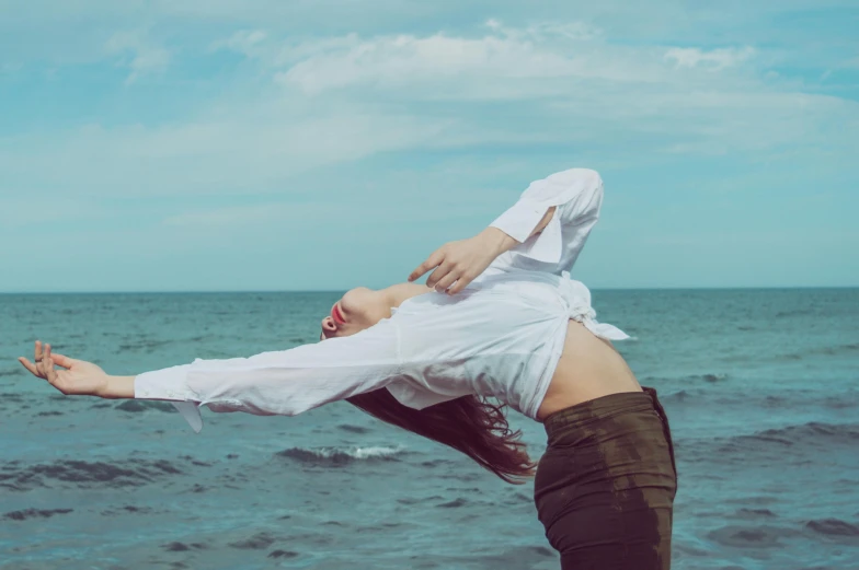 a woman standing on top of a beach next to the ocean, an album cover, pexels contest winner, aestheticism, acrobatic pose, clothed in white shirt, woman holding another woman, [ floating ]!!