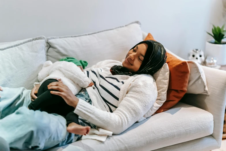 a woman laying on a couch holding a baby, pexels contest winner, hurufiyya, manuka, aida muluneh, casually dressed, also very detailed