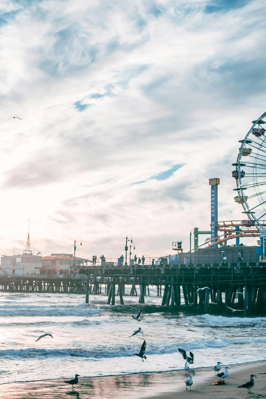 a ferris wheel sitting on top of a beach next to a pier, on the ocean