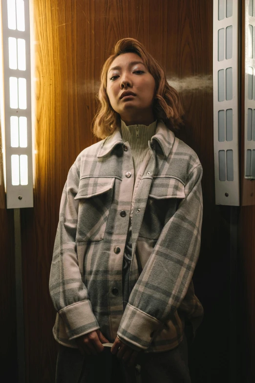 a woman standing in front of a window, an album cover, trending on pexels, hyperrealism, wearing plaid shirt, in the dark elevator, lee madgwick & liam wong, grey clothes