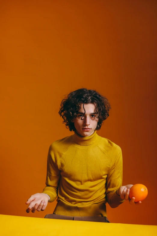 a man sitting at a table with two oranges, an album cover, pexels, wavy hair yellow theme, asher duran, wearing turtleneck, teenage boy