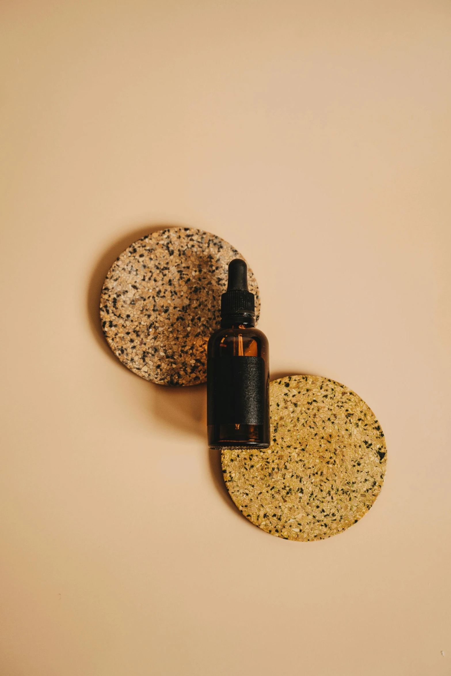 a bottle of essential oil sitting on top of a stone, by Emma Andijewska, on textured disc base, droplets on the walls, sustainable materials, hip modern vibe