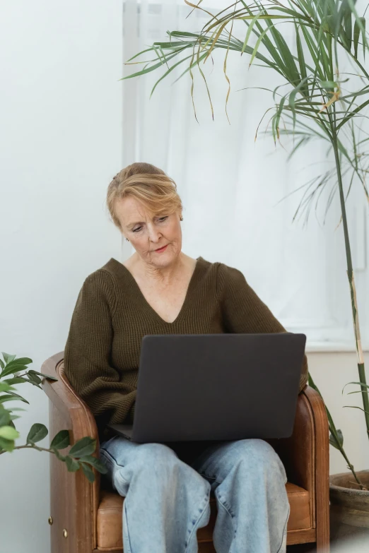 a woman sitting in a chair with a laptop, next to a plant, profile image