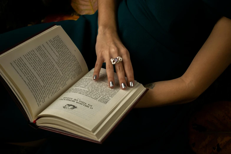 a woman in a blue dress is reading a book, a portrait, pexels contest winner, magic realism, wearing two metallic rings, dramatic product shot, silver and amethyst, wearing jewellery