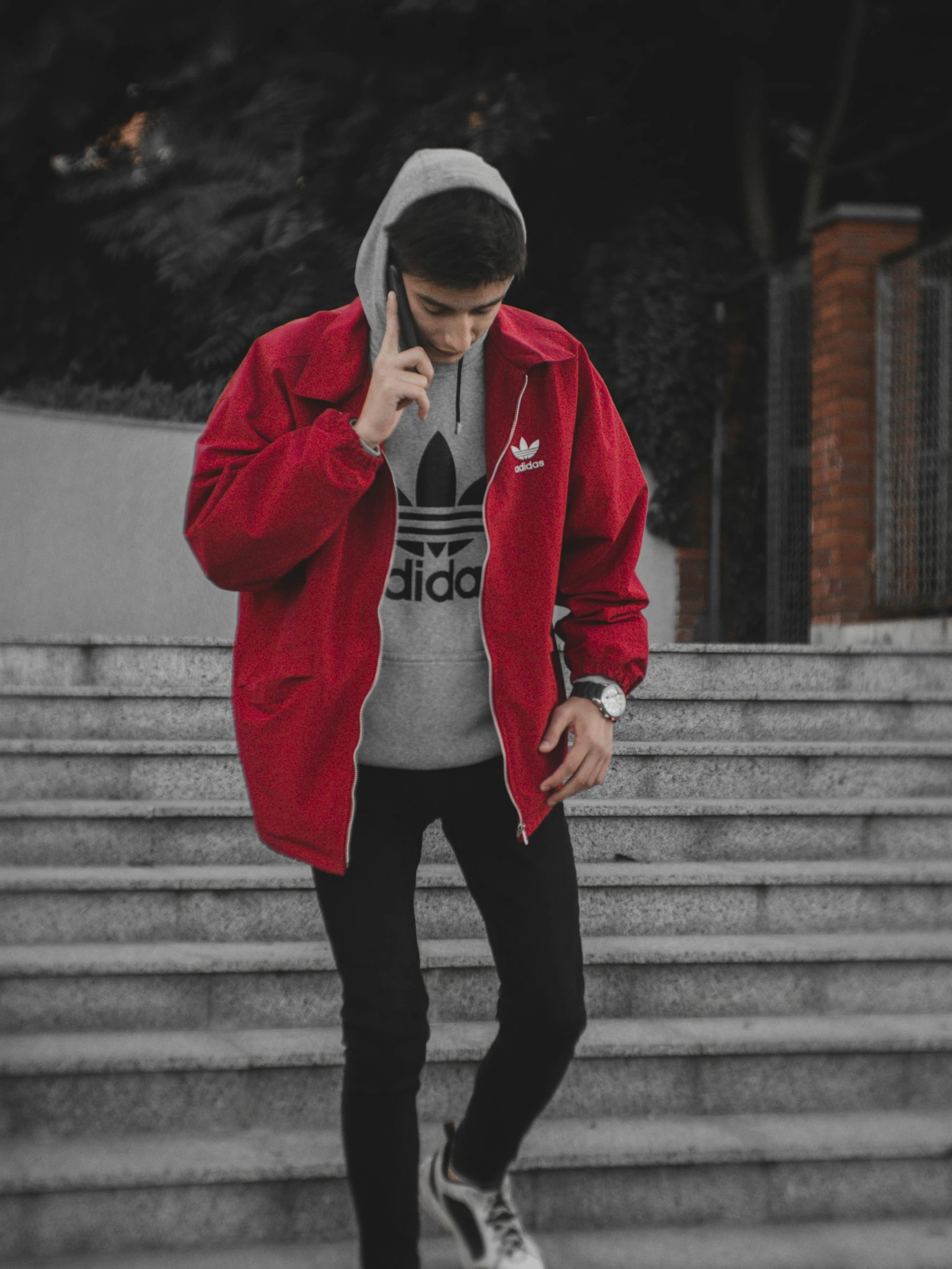 a man in a red jacket talking on a cell phone, a colorized photo, by Alejandro Obregón, unsplash, wearing adidas clothing, grey jacket, menacing pose, ✨🕌🌙