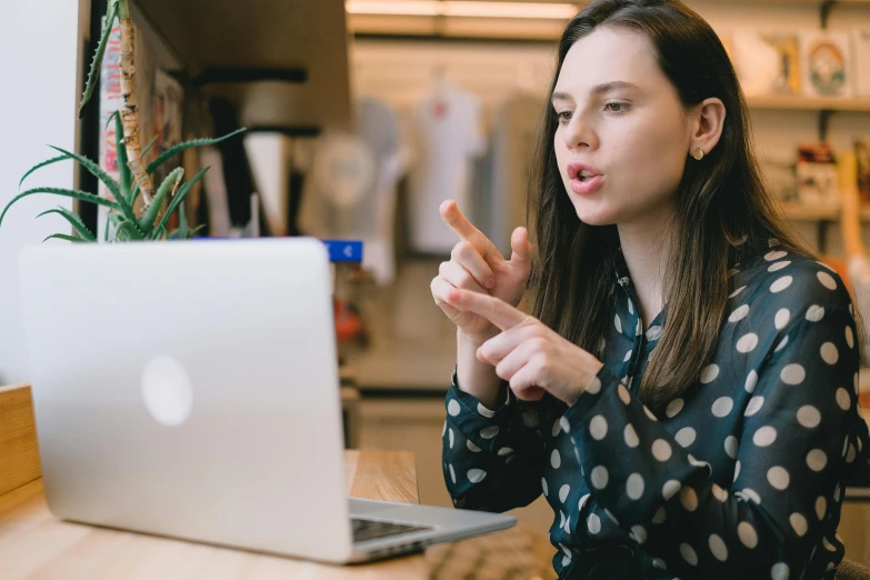 a woman sitting at a table in front of a laptop, trending on pexels, pointing, patterned, surprised, casually dressed