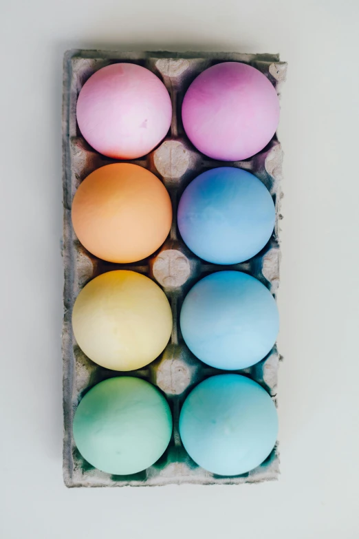 a carton filled with eggs sitting on top of a table, a colorized photo, by Jessie Algie, trending on unsplash, soft rainbow, matte paint colors, spheres, chalk