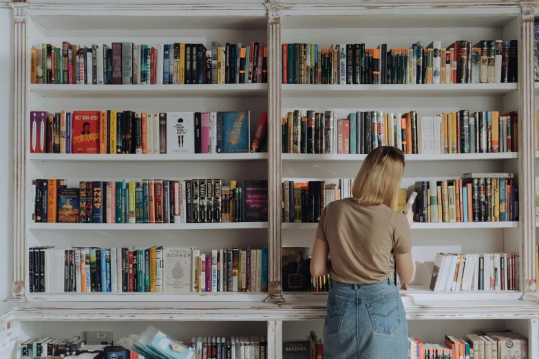 a woman standing in front of a book shelf filled with books, by Carey Morris, pexels contest winner, millennial vibes, with a white background, background image, sydney hanson