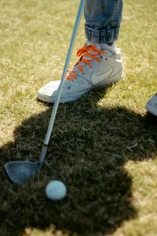 a man standing on top of a green field next to a golf ball, battle shoes, grey orange, mid action swing, thumbnail