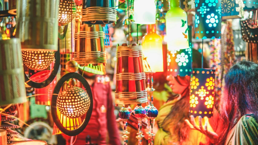 a woman standing in front of a display of lamps, pexels, maximalism, festive colors, india, wind chimes, an orgy of colorful