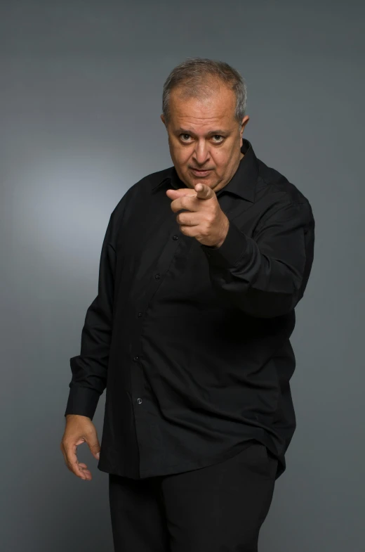 a man in a black shirt pointing at something, inspired by Arthur Sarkissian, les nabis, angry looking at camera, standup comedian, gene espy, press shot