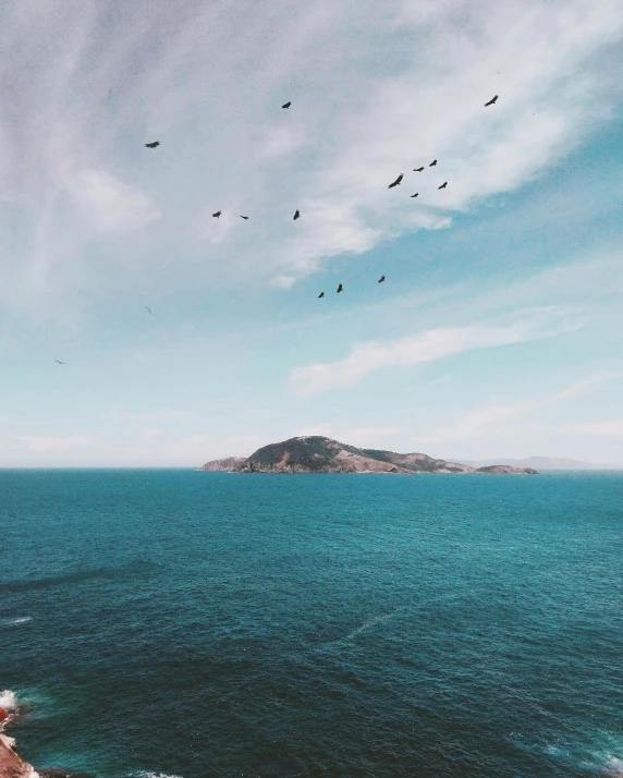 a group of birds flying over a body of water, by Morgan Russell, unsplash contest winner, romanticism, hills and ocean, two medium sized islands, san francisco, slightly tanned