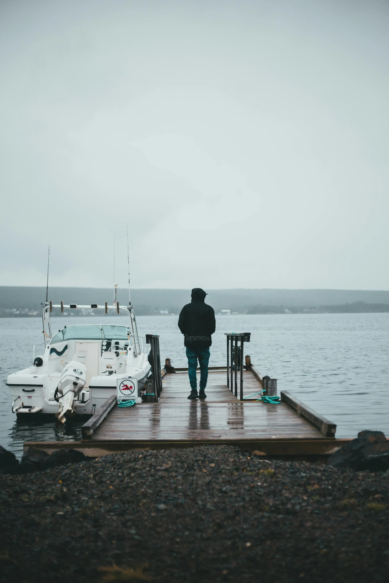 a person standing on a dock next to a body of water, sad men, boat, gray skies, trending photo