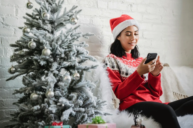 a woman sitting on a couch next to a christmas tree, a photo, pexels, she is holding a smartphone, profile image, wearing festive clothing, flatlay