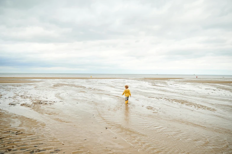a little boy standing on top of a sandy beach, by Arabella Rankin, unsplash, minimalism, yellow raincoat, girl running, landscape photo, dwell