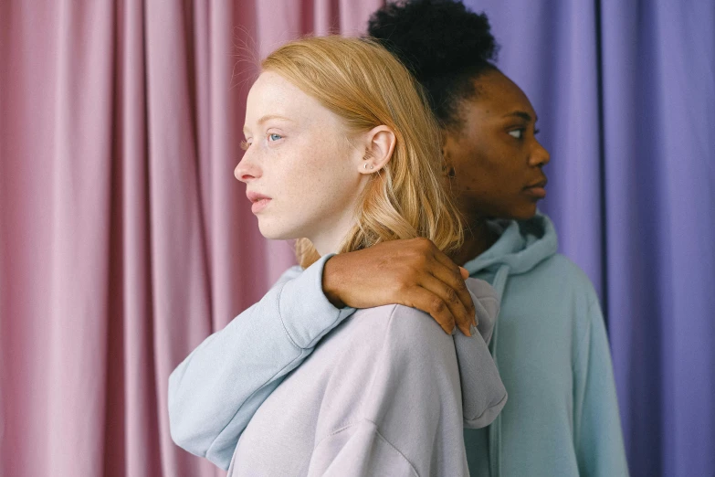 a couple of women standing next to each other, trending on pexels, renaissance, pale pastel colours, girl wearing hoodie, diverse, comforting