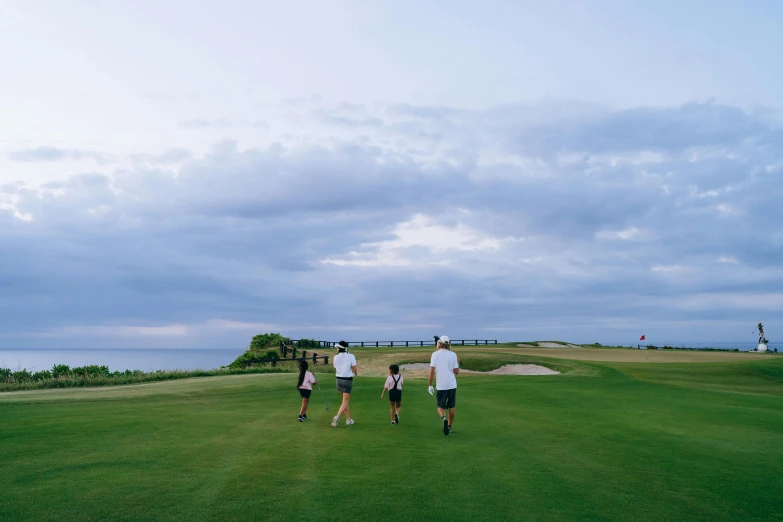 a group of people walking across a lush green field, view of the ocean, wearing golf shorts, instagram picture, children's