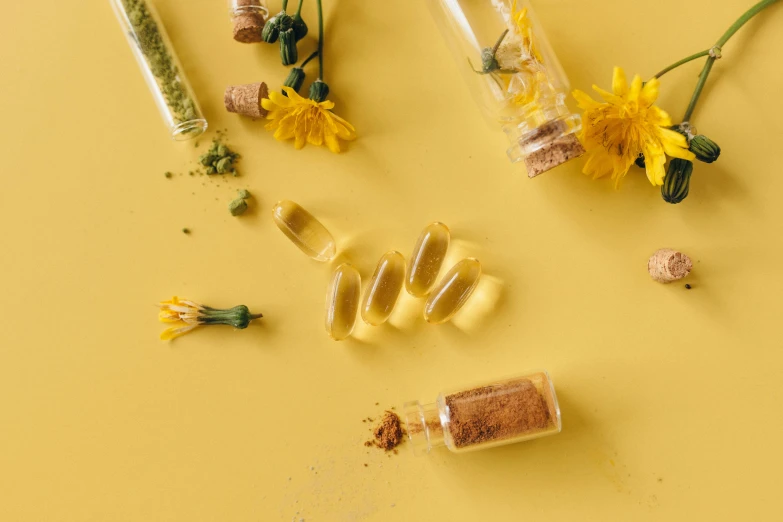 a bunch of pills sitting on top of a yellow surface, a picture, by Julia Pishtar, trending on pexels, herbs, gold flaked flowers, glass vials, detailed product image