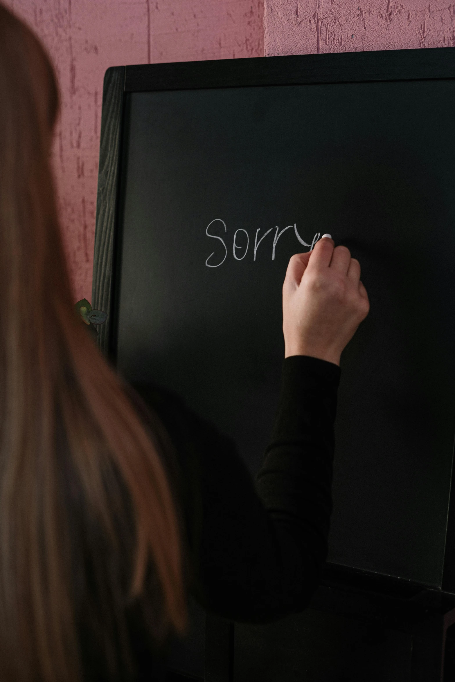 a woman writing on a blackboard in front of a pink wall, by Andries Stock, pexels, still from the the sopranos, facepalm, 1 6 x 1 6, forgiveness