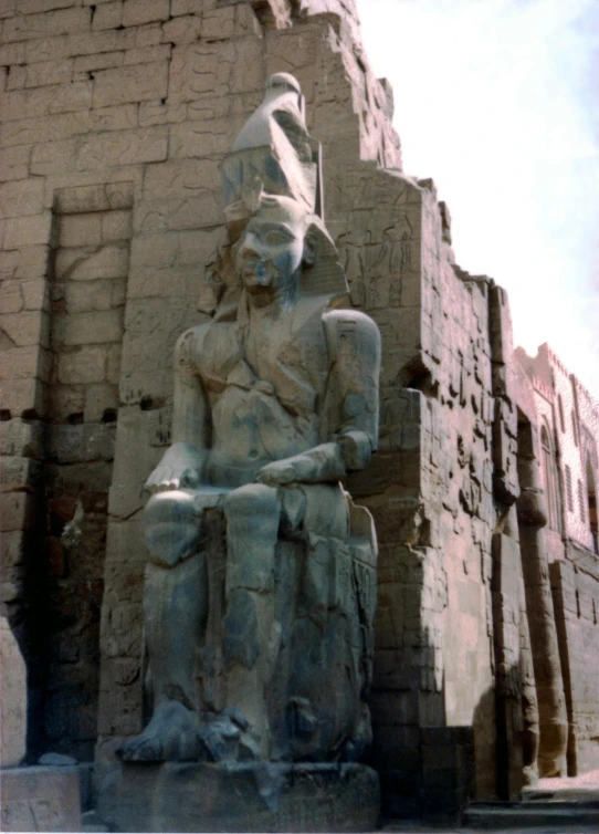 a statue of a man sitting in front of a building, hurufiyya, a 15 foot tall, wearing an egyptian crown, color photo, grey