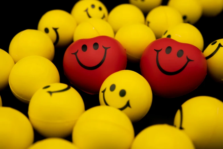 a red ball with a smiley face drawn on it surrounded by yellow balls, by Stefan Gierowski, pexels, toyism, both smiling for the camera, on a dark background, closeup at the faces, thumbnail