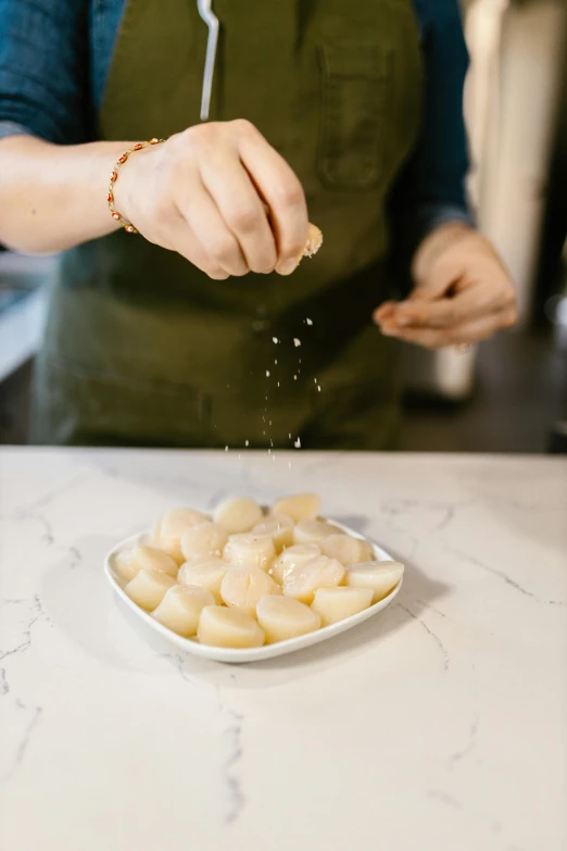 a woman sprinkles salt onto a plate of scallops, inspired by Modest Urgell, unsplash, potatoes, while marble, handcrafted, adi meyers