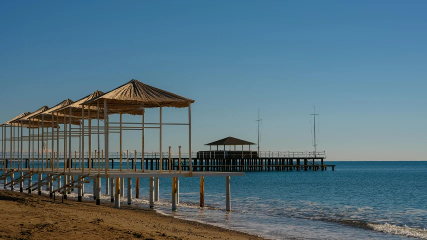 a group of umbrellas sitting on top of a sandy beach, wooden platforms, baris yesilbas, near a jetty, afternoon light