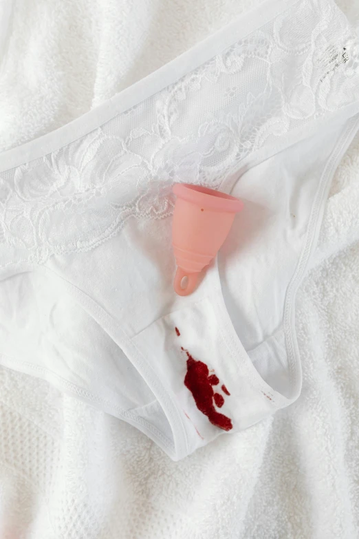 a pair of underwear sitting on top of a bed, blood drop, white and pink cloth, censored, cone