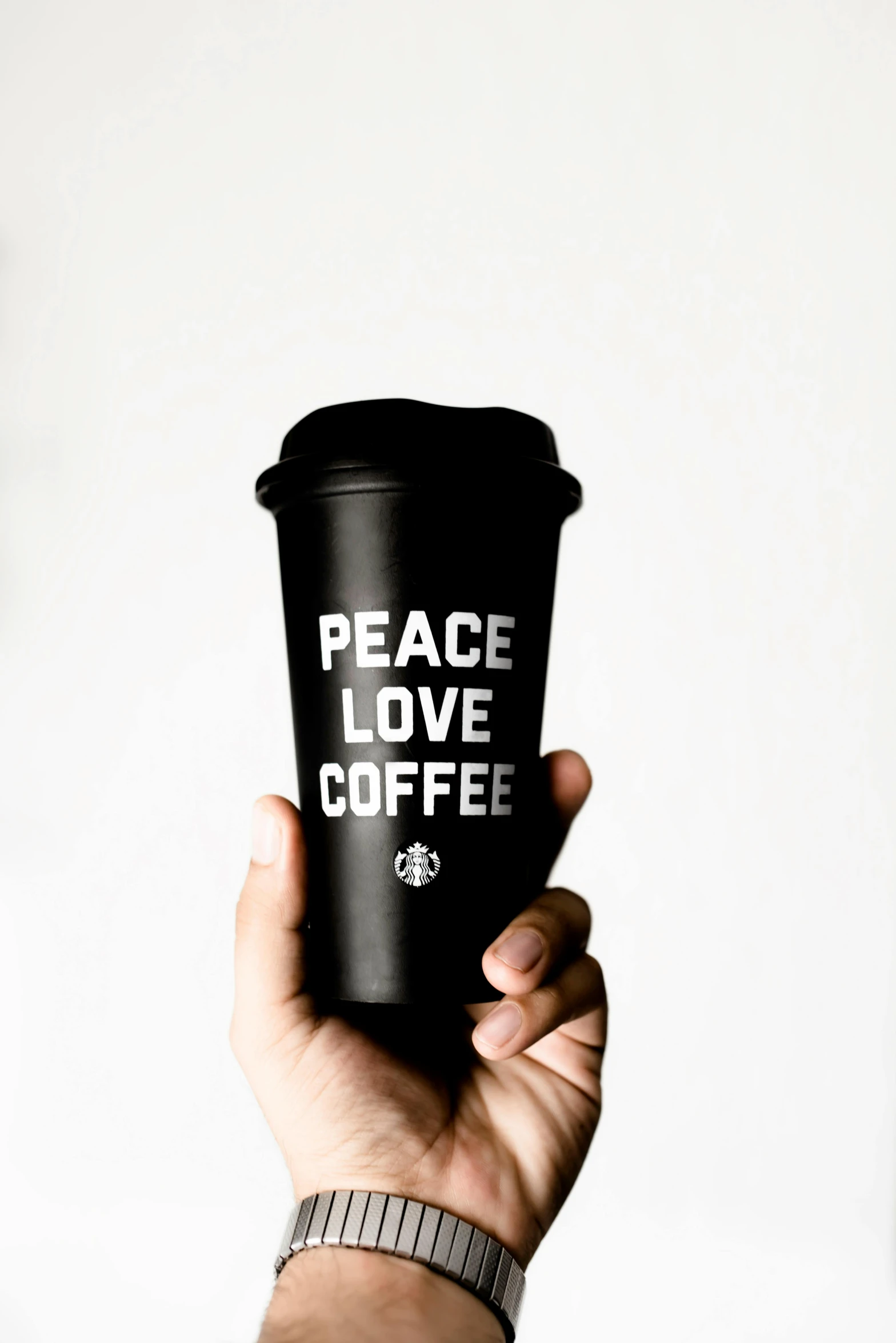 a hand holding a coffee cup that says peace love coffee, a black and white photo, pexels, photorealism, all black matte product, starbucks, set against a white background, dark. no text